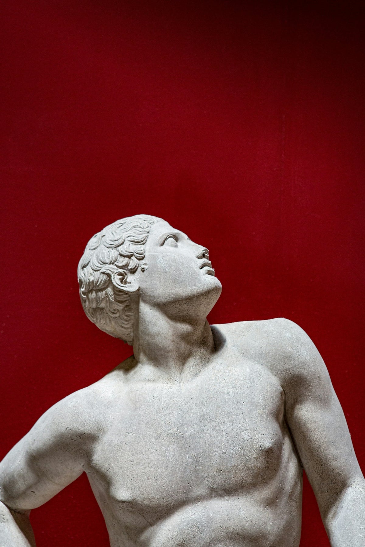 Statue grecque d'homme, le regard levé, sur fond rouge